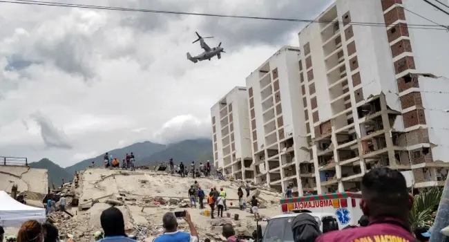28 Haziran 2026'da, ikiz depremlerin ardından Venezuela'nın La Guaira eyaletindeki Caraballeda'da depremden etkilenen bir bölgenin üzerinden bir Osprey uçağı uçuyor. / AFP